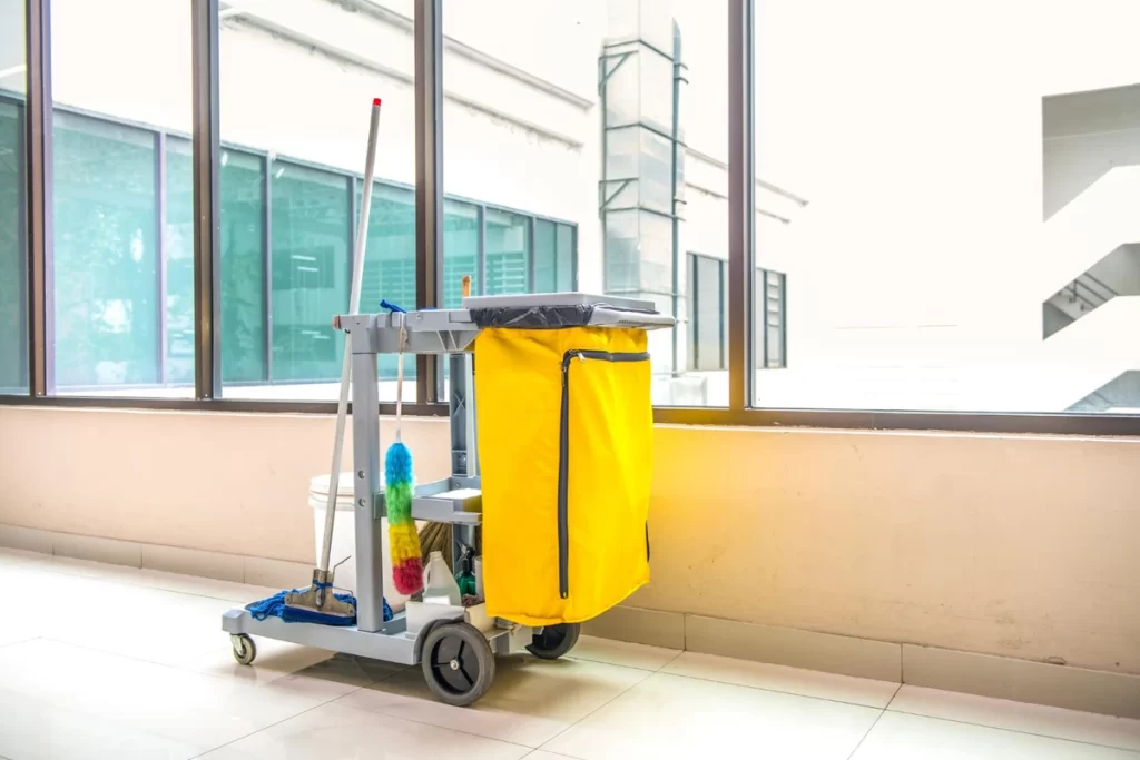 Carrinho de limpeza com equipamentos e sacos em um ambiente iluminado.