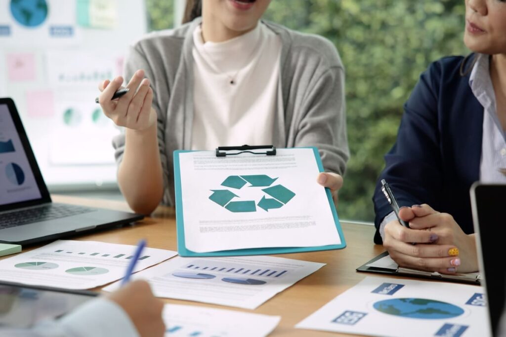 Funcionária apresentando prancheta com o símbolo da reciclagem em reunião