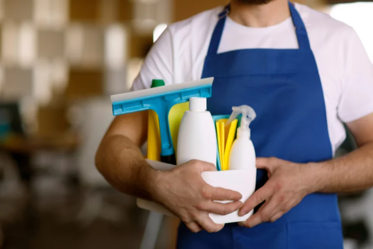Rapaz com camisa branca e avental azul segura produtos de limpeza, ilustrando um artigo sobre gestão de facilities da SuperPro Bettanin.