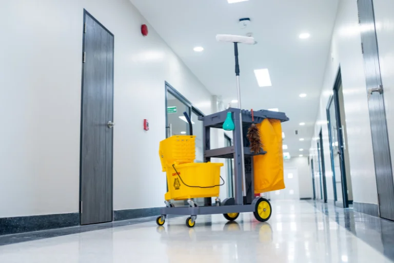 Carrinho de limpeza industrial amarelo localizado no centro de um corredor.