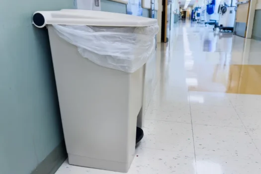 Lixeira plástica branca com saco plástico em corredor hospitalar limpo e iluminado, representando lixo hospitalar de um artigo da SuperPro Bettanin.