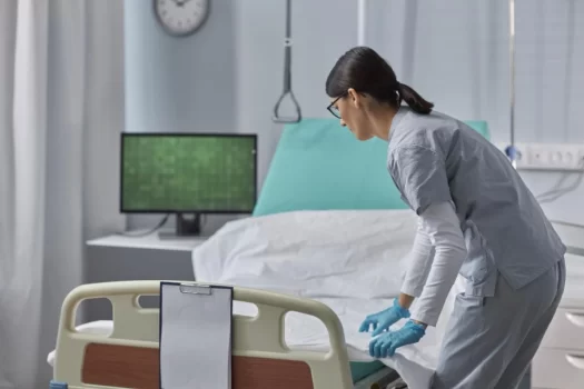 Profissional de limpeza limpando o quarto de um hospital, seguindo o manual de limpeza e desinfecção de superfícies.