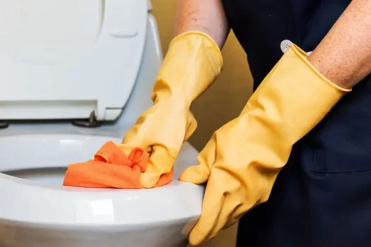 Profissional limpando vaso sanitário com luva e pano multiuso, representando os EPIs para limpeza de banheiros.